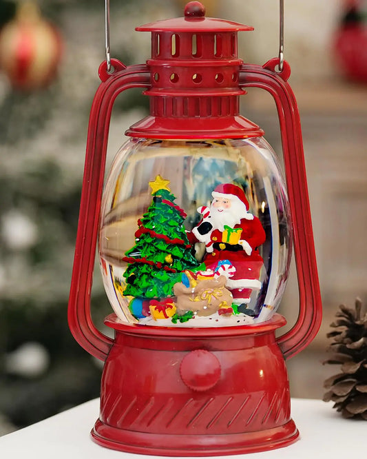 Red lantern-shaped Christmas snow globe with Santa Claus and tree inside, blurred Christmas tree in the background.