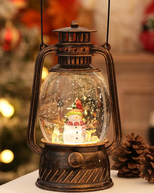 Decorative lantern with a snow globe inside, featuring a snowman and Christmas tree, with a blurred festive background.